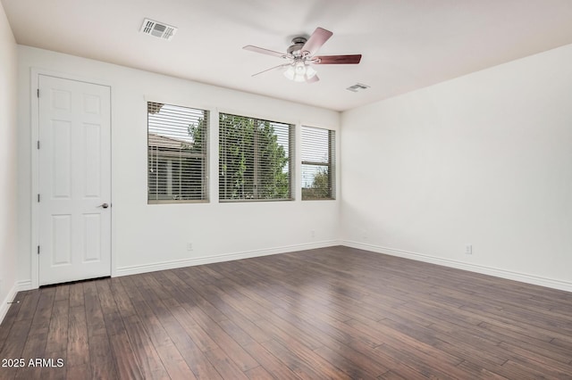 empty room with dark wood-type flooring, a ceiling fan, visible vents, and baseboards