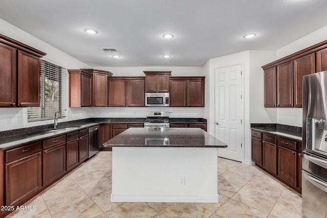 kitchen with a sink, visible vents, appliances with stainless steel finishes, a center island, and dark stone countertops