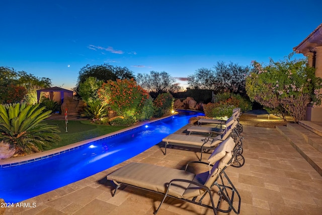 pool at dusk featuring pool water feature and a patio