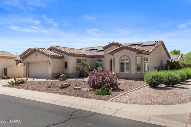 mediterranean / spanish-style house featuring stucco siding, solar panels, a garage, and a tiled roof