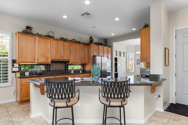 kitchen with freestanding refrigerator, recessed lighting, a breakfast bar area, backsplash, and dark stone countertops