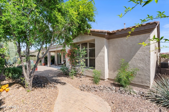 view of front facade featuring stucco siding, a patio area, a tiled roof, and central air condition unit