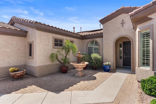 doorway to property with stucco siding, a patio, a tiled roof, and roof mounted solar panels