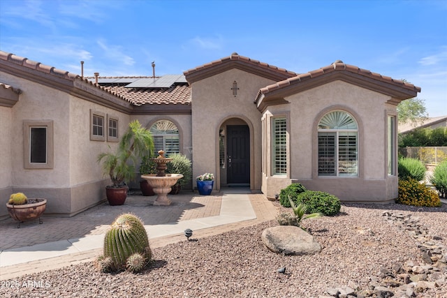 view of front of property featuring stucco siding, roof mounted solar panels, and a tiled roof