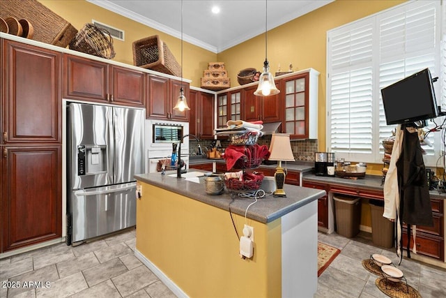 kitchen featuring stainless steel appliances, dark countertops, crown molding, an island with sink, and backsplash