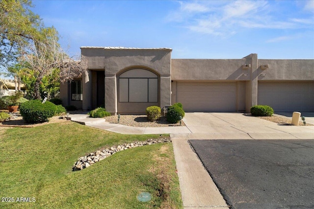 pueblo-style home featuring driveway, an attached garage, a front yard, and stucco siding