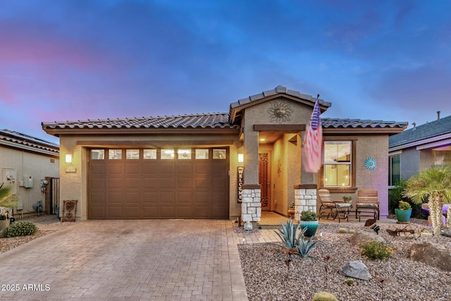 mediterranean / spanish-style home featuring an attached garage, stucco siding, a tile roof, and decorative driveway