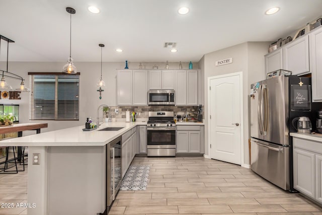 kitchen with appliances with stainless steel finishes, a sink, a peninsula, wine cooler, and backsplash