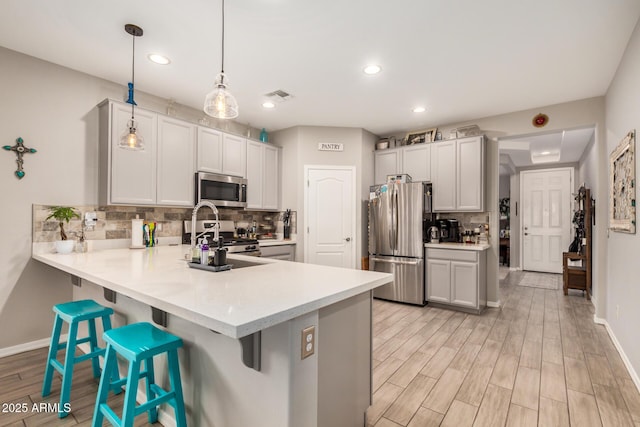 kitchen featuring appliances with stainless steel finishes, light countertops, a peninsula, backsplash, and visible vents