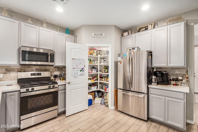 kitchen with visible vents, light wood-type flooring, light countertops, tasteful backsplash, and appliances with stainless steel finishes
