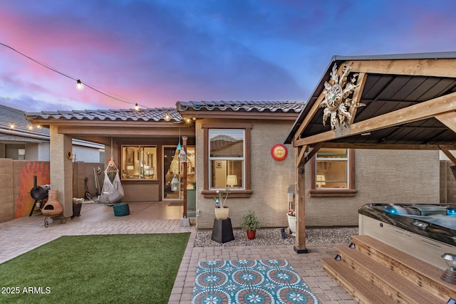 back of property at dusk with fence, a patio, a hot tub, and a tile roof