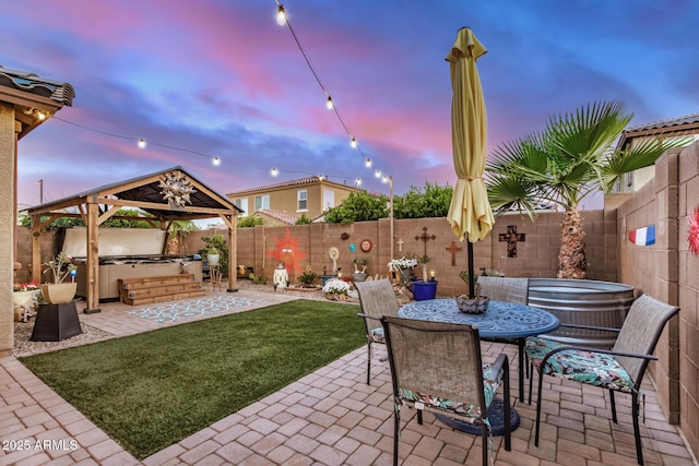 patio terrace at dusk with a gazebo, a fenced backyard, a hot tub, and a lawn