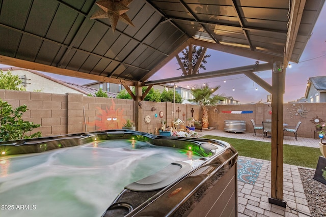 patio terrace at dusk with a hot tub, fence, and a ceiling fan