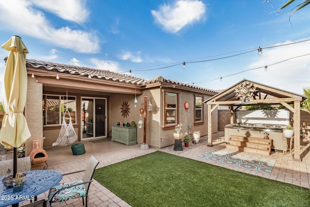 back of property featuring a gazebo, a hot tub, a patio area, and stucco siding