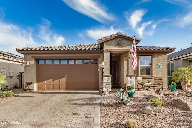 view of front of house featuring a tile roof, decorative driveway, an attached garage, stone siding, and stucco siding