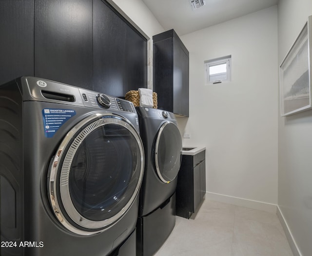 clothes washing area with washer and dryer, cabinets, and light tile floors