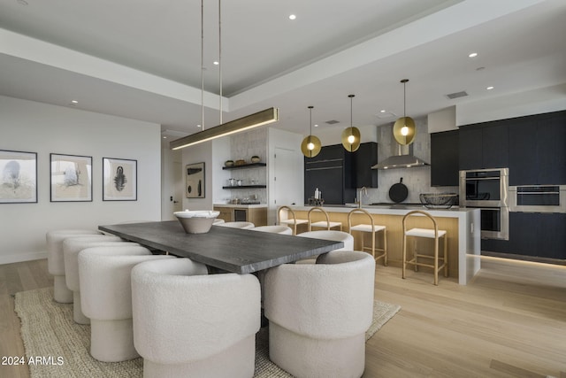 dining space with a tray ceiling, sink, and light wood-type flooring