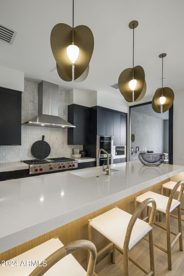 kitchen with stainless steel appliances, hanging light fixtures, backsplash, and wall chimney exhaust hood