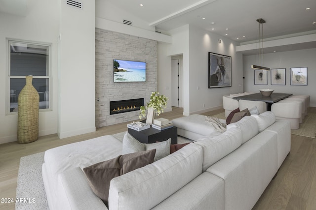 living room with a high ceiling, a stone fireplace, and light wood-type flooring