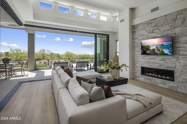 living room featuring a high ceiling, a stone fireplace, and wood-type flooring