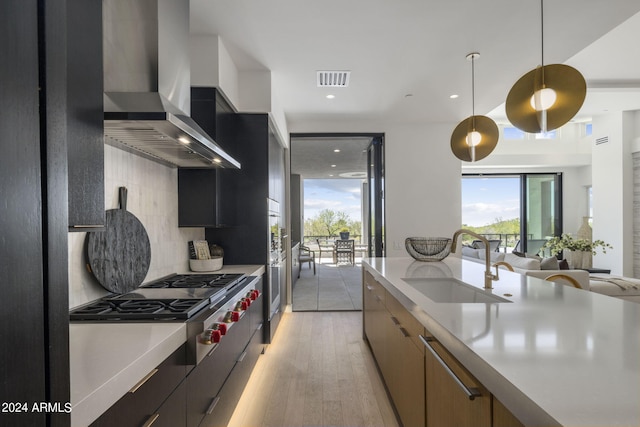 kitchen featuring tasteful backsplash, light wood-type flooring, hanging light fixtures, wall chimney exhaust hood, and sink