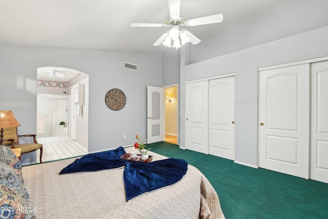 bedroom featuring vaulted ceiling, ceiling fan, two closets, and dark colored carpet