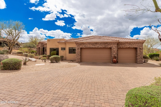 view of front facade with stucco siding, a tile roof, decorative driveway, stone siding, and an attached garage