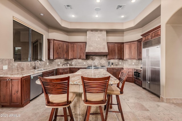 kitchen with a kitchen island with sink, visible vents, premium range hood, and built in appliances