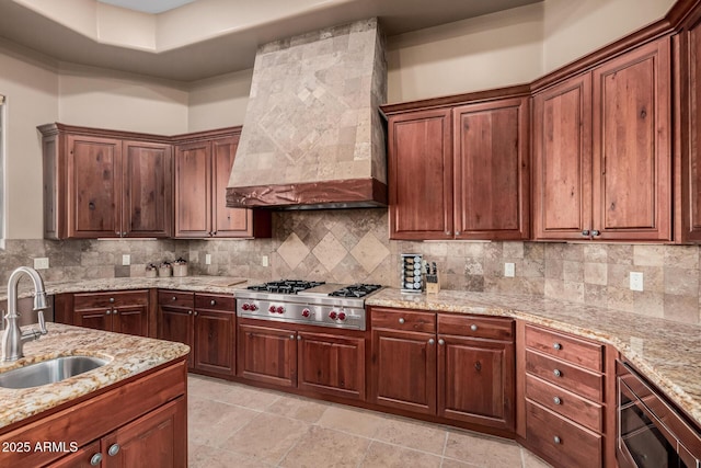 kitchen featuring stainless steel gas cooktop, backsplash, premium range hood, and a sink