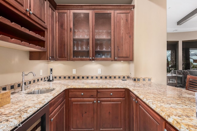 kitchen with beverage cooler, light stone counters, a sink, a peninsula, and glass insert cabinets