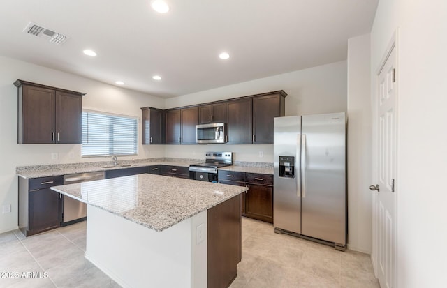 4993 S 254th Dr, Buckeye, AZ 85326 - kitchen with appliances with stainless steel finishes, a sink, dark brown cabinets, a kitchen island, and light stone counters