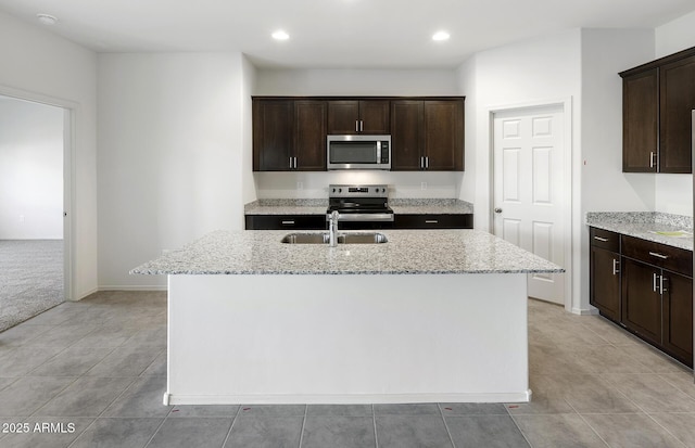 kitchen with stainless steel appliances, light stone counters, a sink, and a kitchen island with sink