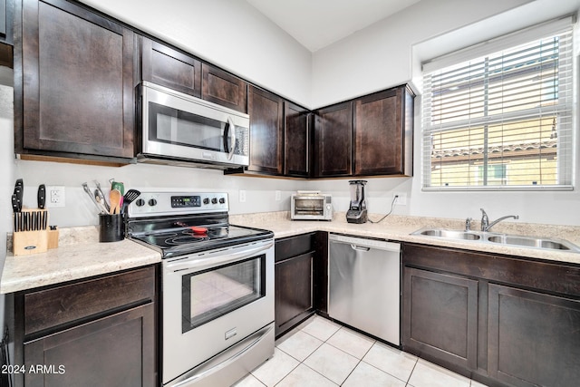 kitchen with appliances with stainless steel finishes, dark brown cabinets, a healthy amount of sunlight, sink, and light tile patterned flooring