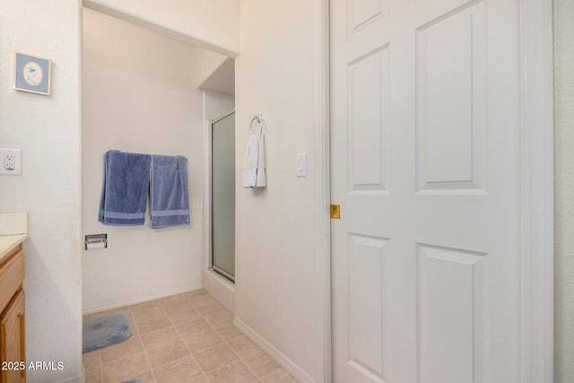 full bath featuring a shower with door, vanity, and baseboards