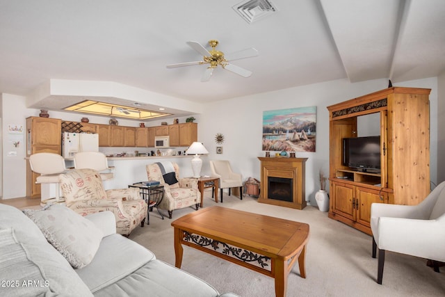 living area featuring ceiling fan, a fireplace, visible vents, and light colored carpet