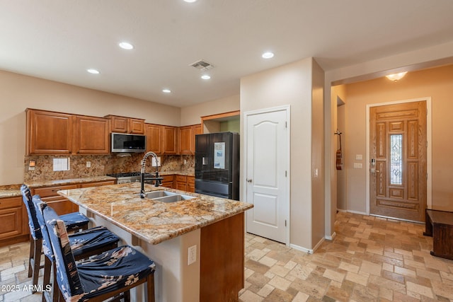 7169 S Dodane Ct, Gilbert, AZ 85298 - kitchen featuring stainless steel microwave, black refrigerator with ice dispenser, a sink, brown cabinetry, and decorative backsplash
