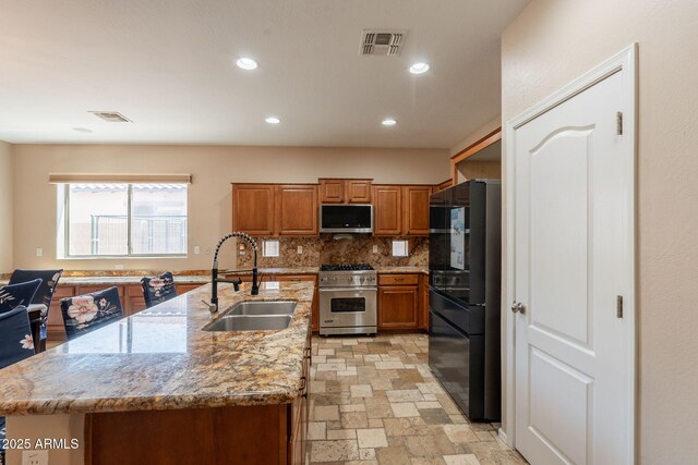 7169 S Dodane Ct, Gilbert, AZ 85298 - kitchen featuring appliances with stainless steel finishes, a sink, brown cabinetry, a center island with sink, and tasteful backsplash