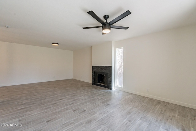 unfurnished living room featuring a brick fireplace, light hardwood / wood-style flooring, and ceiling fan