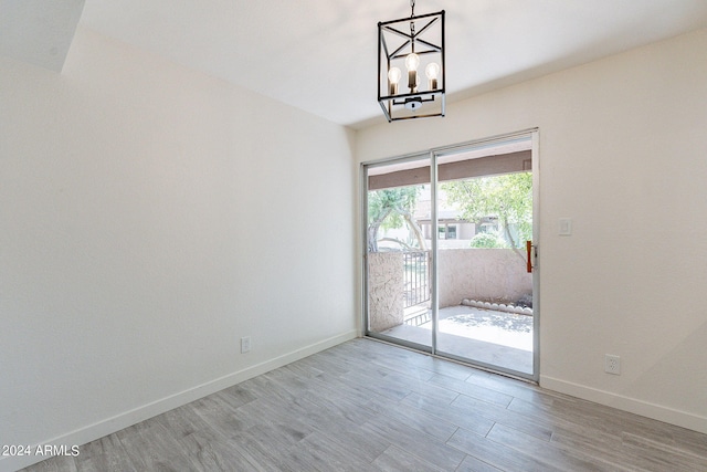 empty room with a healthy amount of sunlight, light hardwood / wood-style flooring, and a notable chandelier