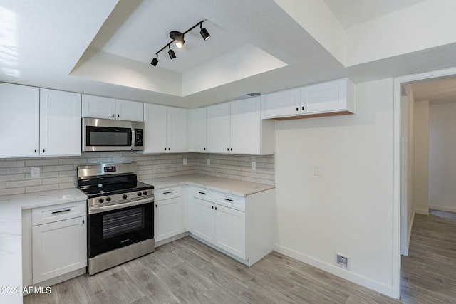 kitchen with appliances with stainless steel finishes, light stone counters, light hardwood / wood-style floors, and white cabinetry