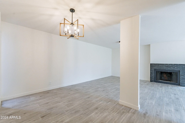 unfurnished living room featuring light wood-type flooring, lofted ceiling, a notable chandelier, and a brick fireplace