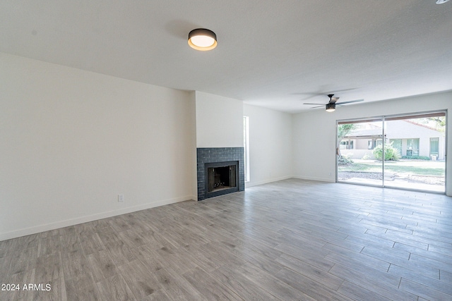 unfurnished living room with a textured ceiling, ceiling fan, a tiled fireplace, and light wood-type flooring