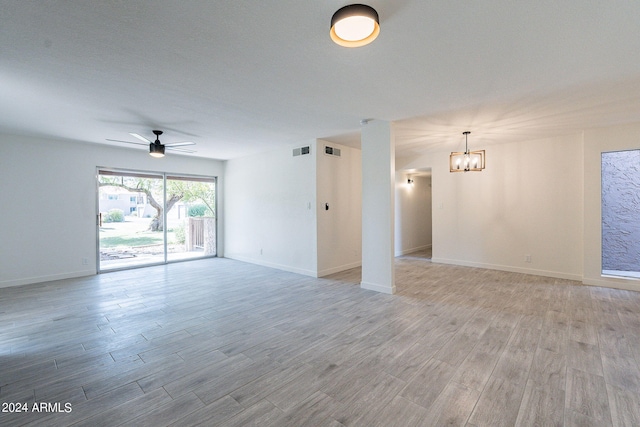 empty room with light wood-type flooring, ceiling fan with notable chandelier, and a textured ceiling