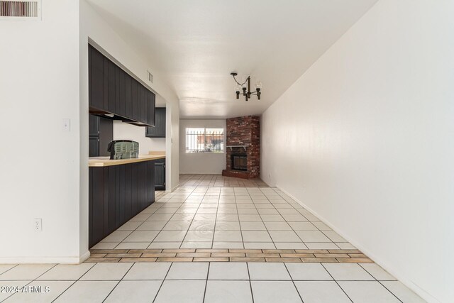 kitchen with light tile patterned flooring, a notable chandelier, and a brick fireplace