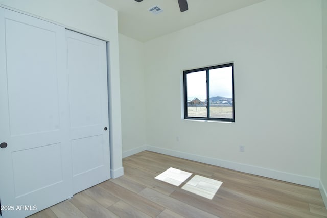 unfurnished bedroom featuring baseboards, light wood-style flooring, visible vents, and a closet