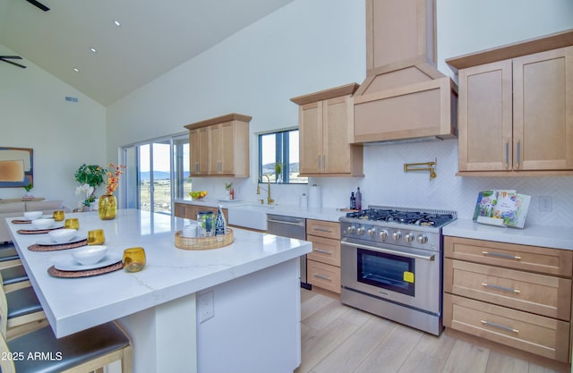 kitchen featuring a sink, backsplash, light brown cabinetry, custom range hood, and stainless steel stove