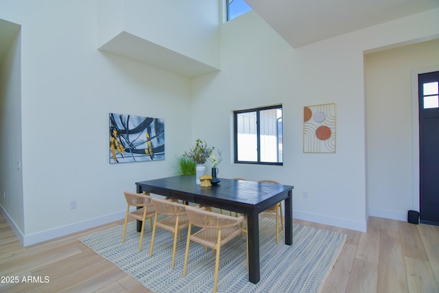 dining space featuring a high ceiling, light wood-style flooring, and baseboards
