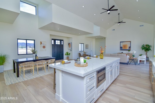 kitchen with white cabinets, stainless steel microwave, light wood-type flooring, open floor plan, and a center island