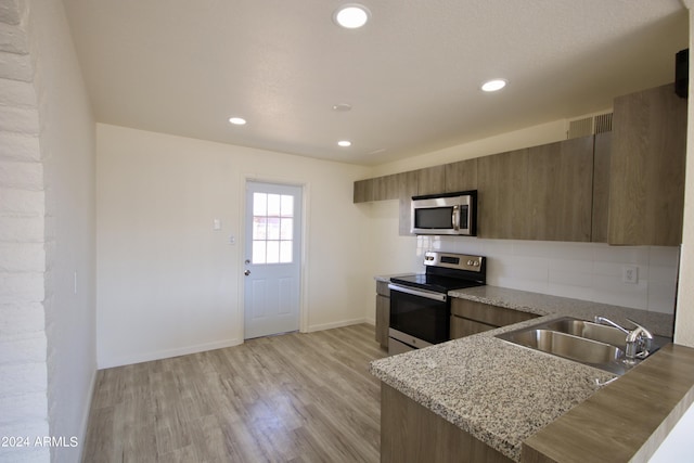 kitchen featuring sink, light hardwood / wood-style flooring, stainless steel appliances, tasteful backsplash, and light stone countertops