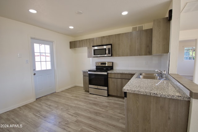 kitchen featuring sink, light hardwood / wood-style flooring, appliances with stainless steel finishes, plenty of natural light, and light stone countertops